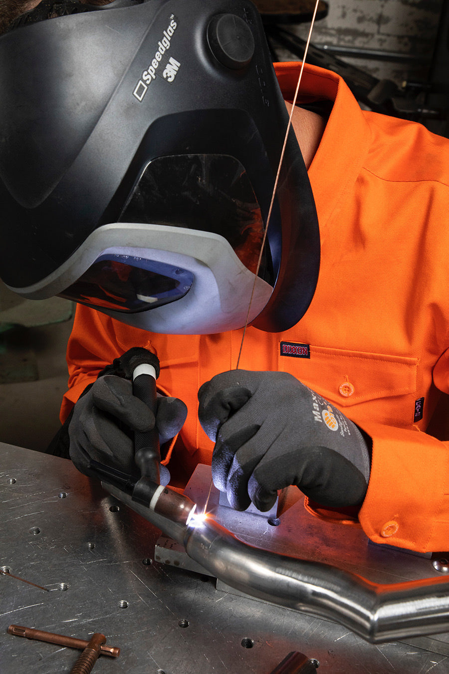 Dixxon Canada. Workforce FR Flannel Safety Orange - Mens. Model wearing the safety orange FR flannel while welding, showcasing its flame-resistant properties and durable design for hazardous work environments.